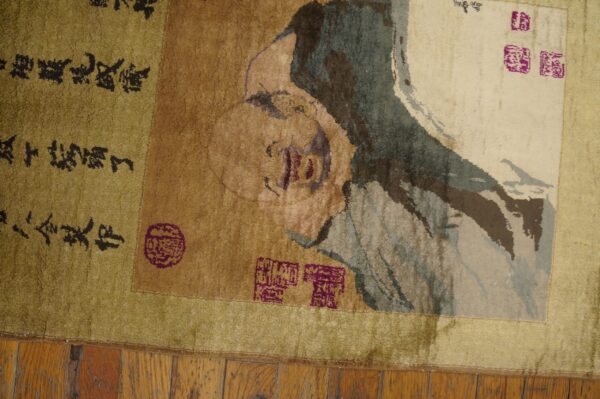 Distressed green, tan, and cream rug featuring a figure portrait, calligraphy, and magenta seal motifs rests on wood floor.