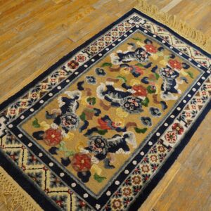 Small gold rug with navy border and colorful stylized animal motifs sits on distressed hardwood floor.