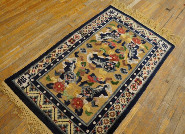 Small gold rug with navy border and colorful stylized animal motifs sits on distressed hardwood floor.