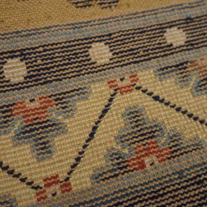 Woven rug detail showing nubby texture and a geometric pattern in tan, navy, light blue, and red.