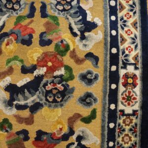 Gold rug with colorful raised motifs and floral border details rests on distressed yellow wood flooring.