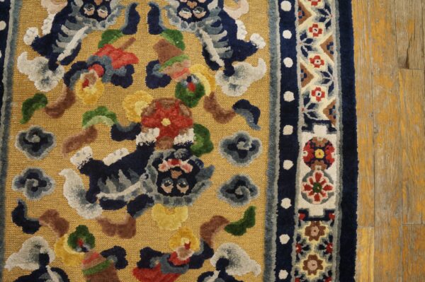 Gold rug with colorful raised motifs and floral border details rests on distressed yellow wood flooring.