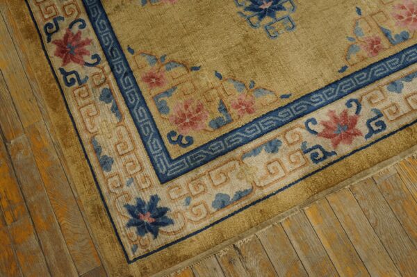 Gold rug with detailed blue and pink floral border lies on distressed yellow-toned wood flooring.