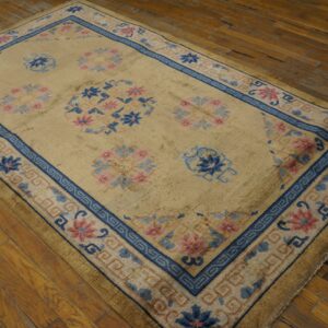 Tan rug with blue and rose floral motifs and geometric borders placed on worn wood planks.