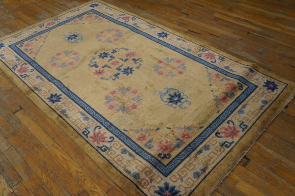Tan rug with blue and rose floral motifs and geometric borders placed on worn wood planks.