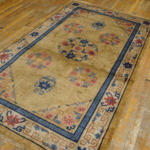A muted gold rug featuring navy and pink floral patterns is placed on distressed yellow wood floorboards.
