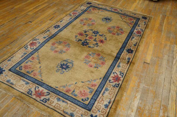 A muted gold rug featuring navy and pink floral patterns is placed on distressed yellow wood floorboards.