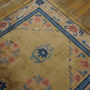 A tan rug with bright blue and pink floral borders rests on rustic wooden flooring.