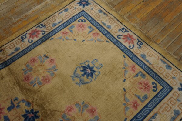 A tan rug with bright blue and pink floral borders rests on rustic wooden flooring.