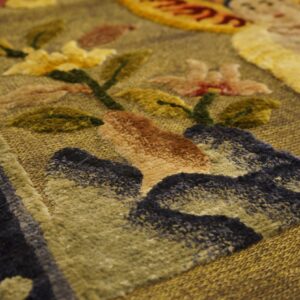 Sculpted rug texture shows a golden background with raised dark blue, rust, green, and yellow floral patterns.