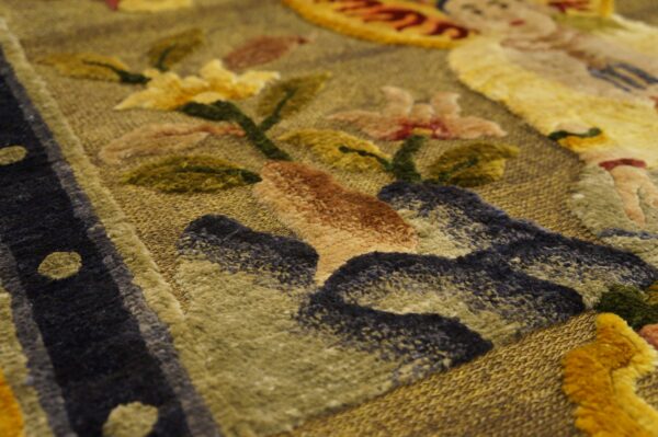Sculpted rug texture shows a golden background with raised dark blue, rust, green, and yellow floral patterns.