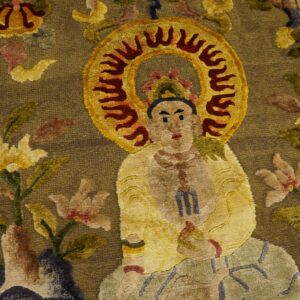 Detailed view of a rug with a seated figure and flaming halo on a textured brown-gold field surrounded by multicolor florals.