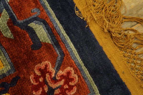 Textured rug detail in rust and navy borders a gold flatweave edge with thick fringe on wood flooring.