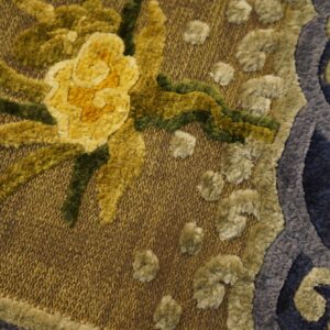 Textured rug detail showing yellow and green flowers, blue scrollwork, and a woven golden background.