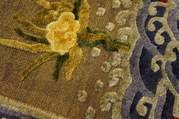 Textured rug detail showing yellow and green flowers, blue scrollwork, and a woven golden background.