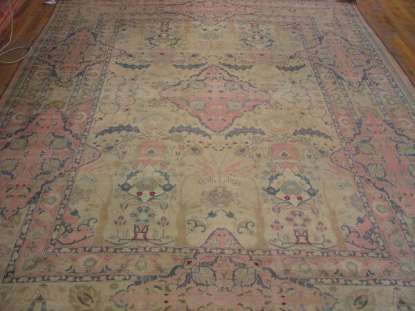 Muted beige, pink, and blue ornate rug featuring a central medallion on wide plank wood flooring.