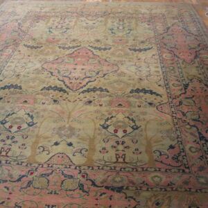 Ornate rug with a beige field, pink border, and blue botanical pattern covering most of a wood plank floor.