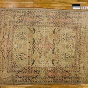 Large pale beige rug with a faded pink, dark blue, and green floral medallion on wood floors.