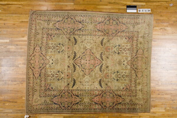 Large pale beige rug with a faded pink, dark blue, and green floral medallion on wood floors.