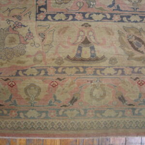Ornate traditional rug detail showing beige and dusty pink floral patterns and complex borders on visible wood floors.