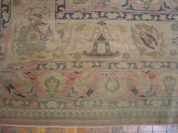 Ornate traditional rug detail showing beige and dusty pink floral patterns and complex borders on visible wood floors.