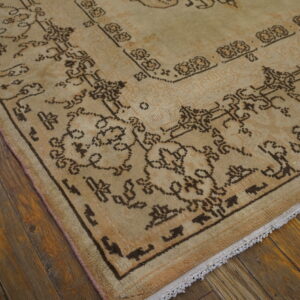The corner of a faded beige rug with dark brown geometric patterns rests on dark hardwood planks.