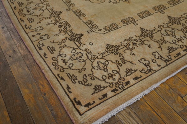 The corner of a faded beige rug with dark brown geometric patterns rests on dark hardwood planks.