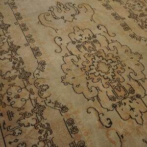 A distressed tan rug with dark brown traditional motifs rests on dark wood plank flooring.