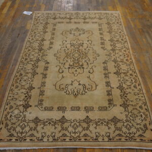 Light beige rug with dark brown traditional curvilinear patterns rests on distressed hardwood flooring.