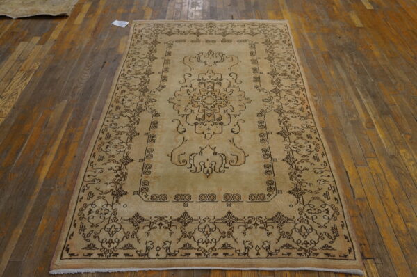 Light beige rug with dark brown traditional curvilinear patterns rests on distressed hardwood flooring.