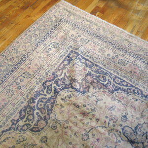 Corner of a faded traditional rug featuring navy and blush floral designs on glossy hardwood planks.