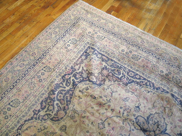 Corner of a faded traditional rug featuring navy and blush floral designs on glossy hardwood planks.