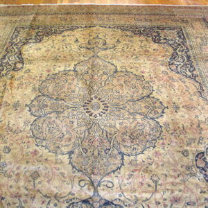 Gold and navy traditional rug with a complex central medallion and border resting on wood flooring.