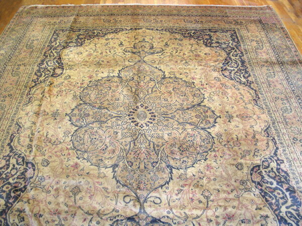 Gold and navy traditional rug with a complex central medallion and border resting on wood flooring.