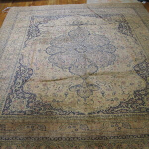 Ornate traditional rug in muted beige, indigo, and pale rose colors on a hardwood floor.