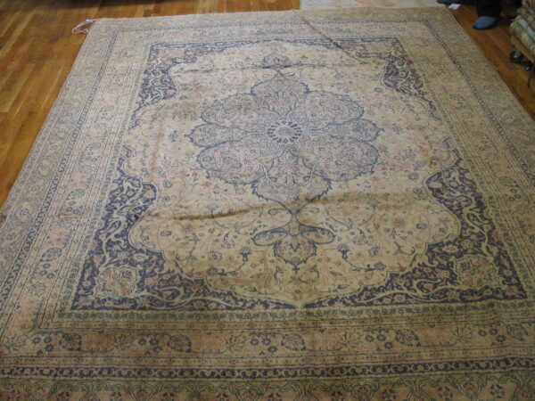 Ornate traditional rug in muted beige, indigo, and pale rose colors on a hardwood floor.