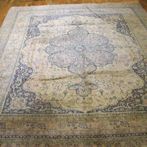 Beige rug with a large navy floral medallion and rose accents on polished wood floor.