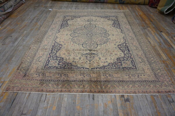 Low-pile traditional rug in beige, navy, and pale pink colors on distressed wood flooring.