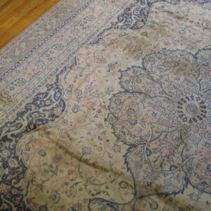 Faded beige rug featuring dark blue and pink traditional floral pattern next to polished wood planks.