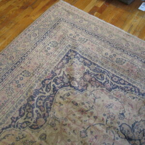 A beige rug with dark blue and pink classical floral patterns lays on a warm wood floor.
