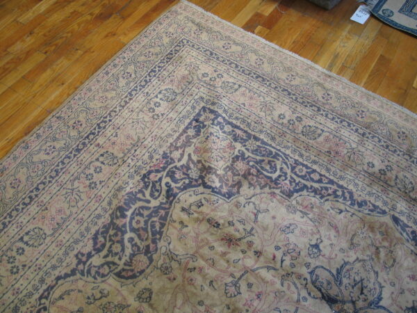A beige rug with dark blue and pink classical floral patterns lays on a warm wood floor.