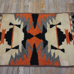 Geometric looped rug in cream, bright orange, black, and gray on weathered wood floorboards.