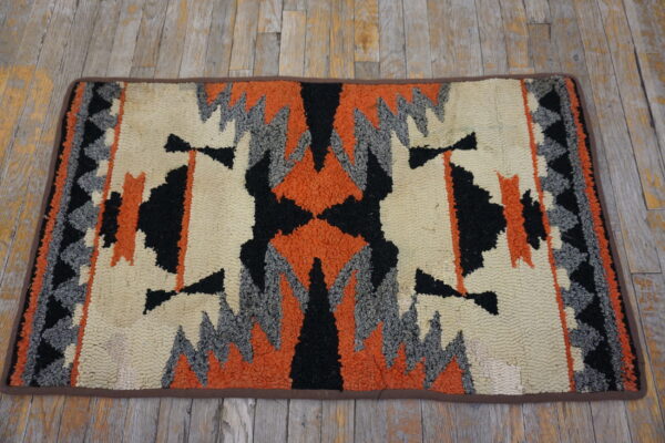 Geometric looped rug in cream, bright orange, black, and gray on weathered wood floorboards.