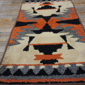 Textured runner rug featuring geometric Southwestern designs in orange, cream, black, and gray on rustic wood flooring.
