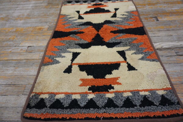 Textured runner rug featuring geometric southwestern designs in orange, cream, black, and gray on rustic wood flooring.