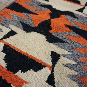 Textured cream, black, orange, and gray rug with geometric designs displayed on wood flooring.