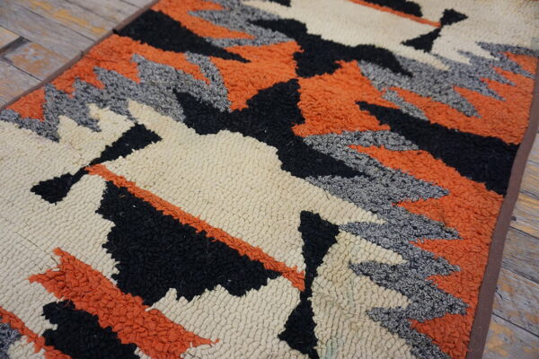 Textured cream, black, orange, and gray rug with geometric designs displayed on wood flooring.