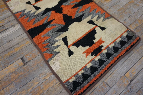 Loop-textured rug runner with black, orange, gray, and cream geometric patterns on distressed wood.