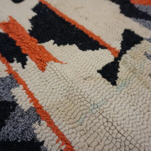 Textured rug detail with creamy looped pile and abstract designs in shaggy black, gray, and orange.