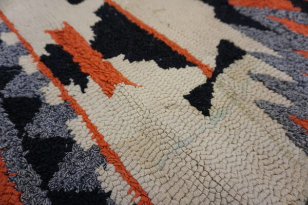 Textured rug detail with creamy looped pile and abstract designs in shaggy black, gray, and orange.